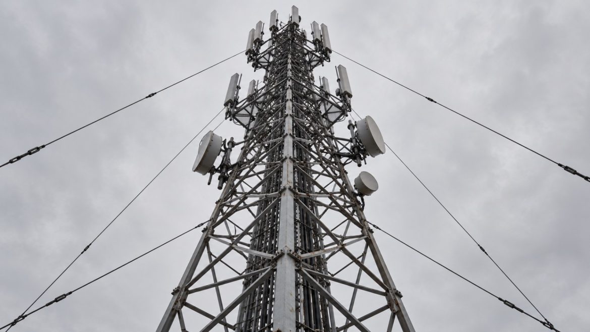 Funkmast mit Antennen und Richtfunkschüsseln von unten gegen grauen Himmel